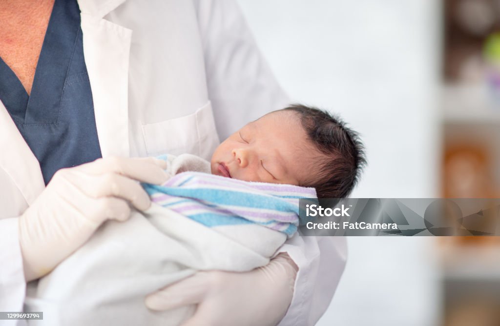 Doctor holding newborn baby A doctor is holding a newborn baby at the hospital. They baby is sleeping. Newborn Stock Photo