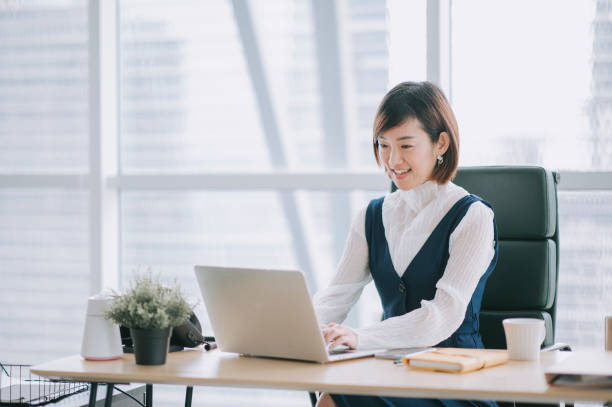 asian chinese beautiful female manager working using her laptop typing in the office asian chinese beautiful female manager working using her laptop typing in the office asian motivated at work stock pictures, royalty-free photos & images