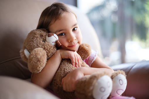 Pretty little girl holding plush teddies in bright children room