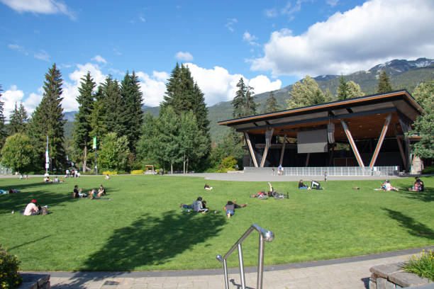 le persone sono sedute sul prato verde in una giornata di sole a whistler village con montagne sullo sfondo - urban scene canada city horizontal foto e immagini stock