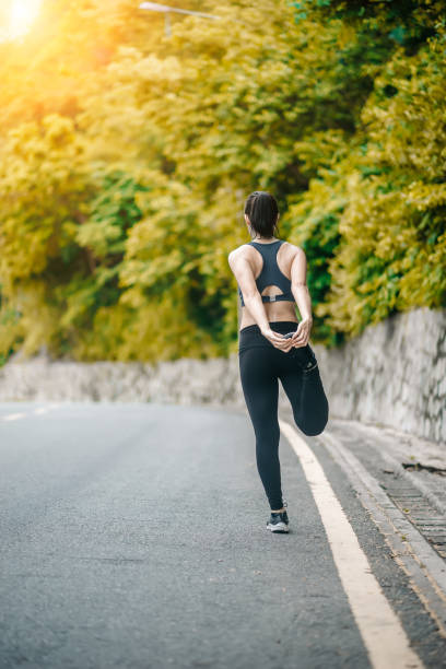 istock Asian fitness runner body closeup doing warm-up routine on beach before running, stretching leg muscles with standing single knee to chest stretch. Female athlete preparing legs for cardio workout. 1299707705