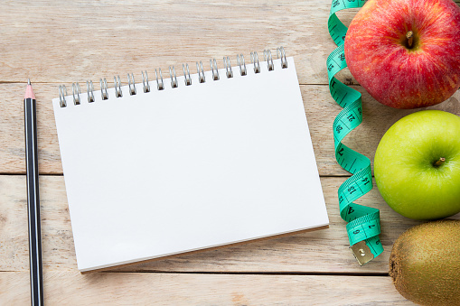 Top view with measuring tape,apple,pencil and notebook on wood table background.Concept for diet and healthcare, nutrition or medical insurance