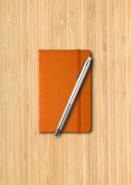 istock Orange closed notebook with a pen on wooden background 1299716189