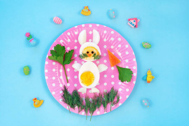 istock Breakfast idea for kids. Bunny rabbit made of boiled eggs on pink plate, blue background, top view. 1299716412