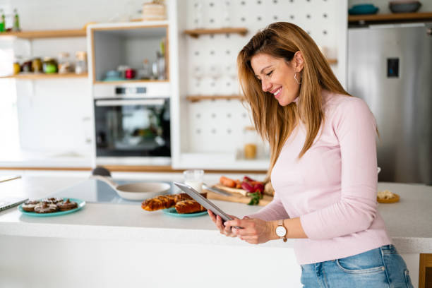 istock Smiling young woman with tablet in the kitchen 1299718726