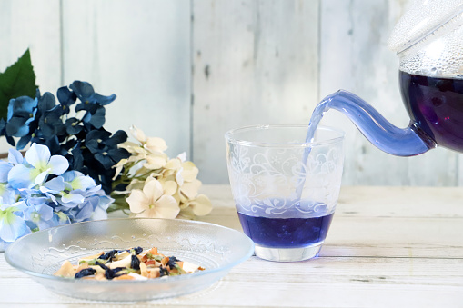 Poring bright blue butterfly pea herb tea to a glass from glass tea pot