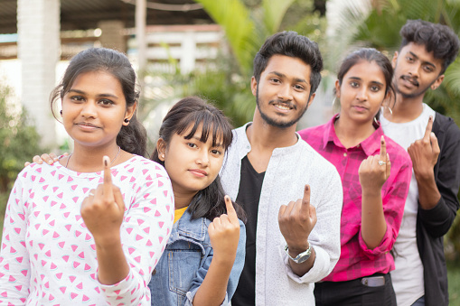 Group of teenager friends showing ink marked fingers outside polling station or booth after casting votes - Concept of Indian election or vote casting system