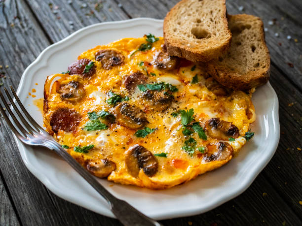 Continental breakfast -  scrambled eggs with sausages, champignons and toasts on wooden table