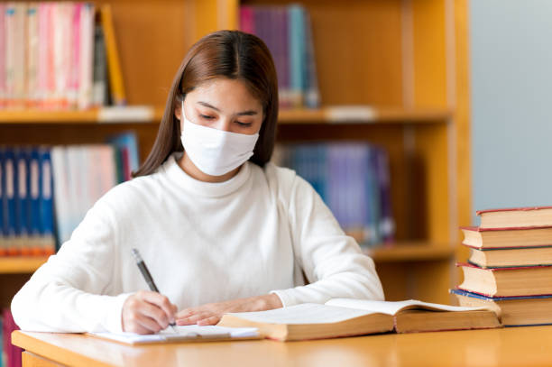 istock Female college student wearing a mask does homework at the university library. 1299728001