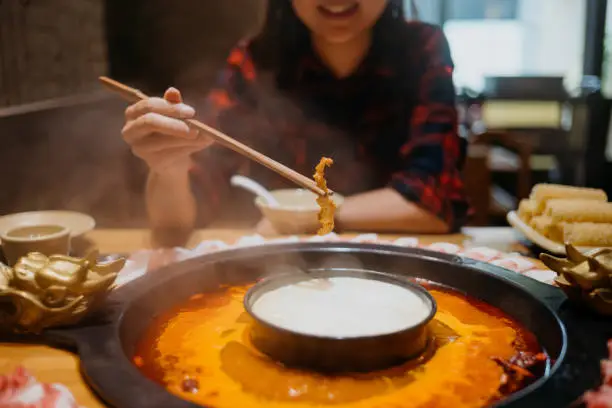 Image of an Asian Chinese woman eating chinese hot pot in a restaurant