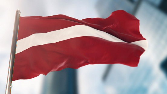 National Flag of Latvia Against Defocused City Buildings