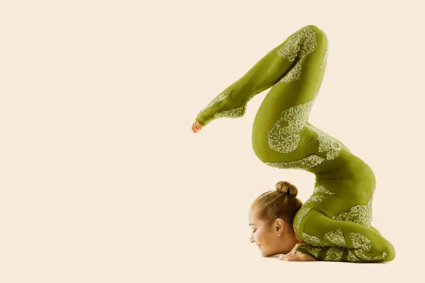 Contortionist Flexible Circus Performer, Acrobat Dancer in Green Costume, Yoga Woman Gymnast Backwards Pose Beige Studio Background