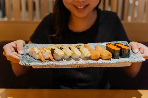 Image of a happy Asian Chinese woman holding a plate of sushi set