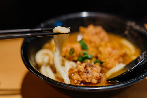 Close up a bowl of curry udon and eating with a chopsticks