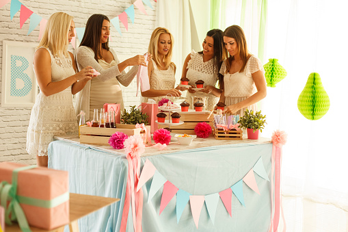 Candid shot of four young women enjoying delicious cupcakes on their pregnant friend's baby shower.