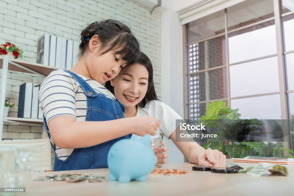 Mother is teaching daugther on financial saving and planing using saving jar and piggy bank with real moner, for Money and wealth education concept. Family Stock Photo