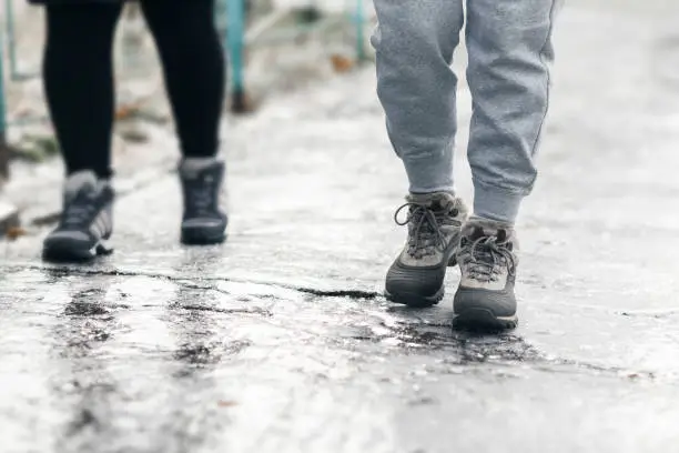 Pedestrians glide along the icy sidewalk. Winter ice on footpaths.