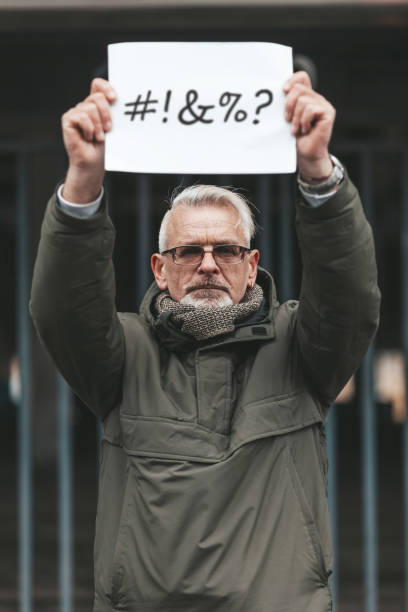 istock Angry and disgruntled mature man protesting with placard. Swearing and cursing. Outraged activist 1299739887