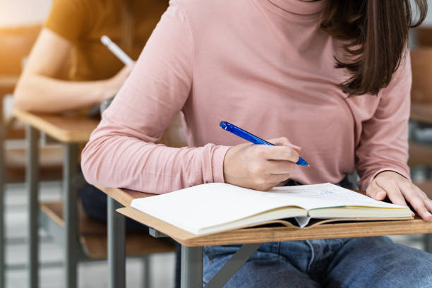 istock Close-up of the university students writing notes on the notebook in the classroom while listening and studying the lecture. Close up of woman's hands writing on notepad placed on wooden desktop 1299740383