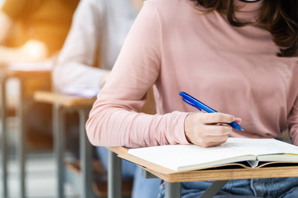 istock Close-up of the university students writing notes on the notebook in the classroom while listening and studying the lecture. Close up of woman's hands writing on notepad placed on wooden desktop 1299740471