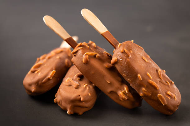 Chocolate ice cream with almonds on a wooden stick in chocolate glaze on dark background Chocolate ice cream with almonds on a wooden stick in chocolate glaze on a dark background sticky photos stock pictures, royalty-free photos & images