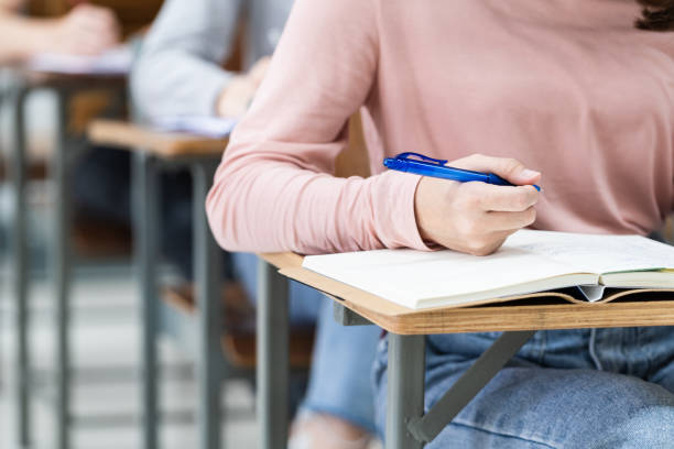 istock Close-up of the university students writing notes on the notebook in the classroom while listening and studying the lecture. Close up of woman's hands writing on notepad placed on wooden desktop 1299742522