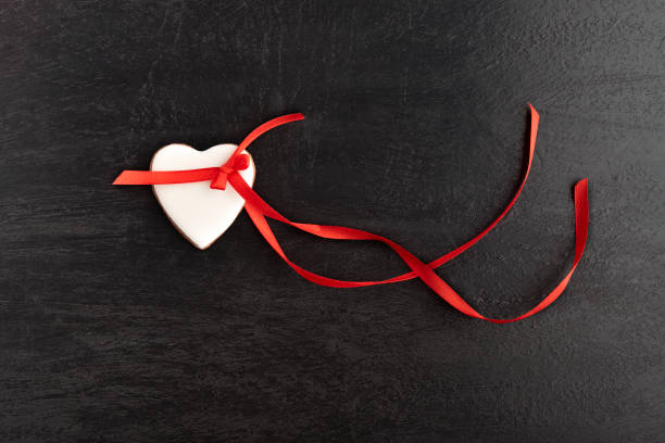 istock White heart shaped cookies with icing and red ribbon on black background. 1299746146