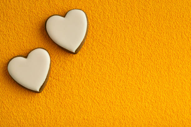istock Two white heart shaped cookies with sugar icing on yellow background. Space for text. Valentines day 1299746231