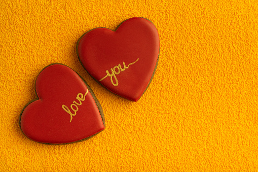 Two heart-shaped cookies with red sugar icing and inscription LOVE YOU, yellow background. Copy space.