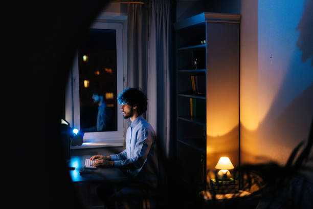 istock Remote view of young freelancer working on computer and typing text on wireless keyboard at late night 1299747382