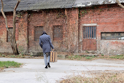 Rear view of man carrying his suitcase while walking away.