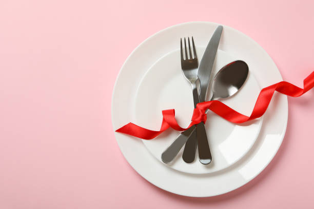 istock Plates with cutlery and red bow on pink background 1299749106