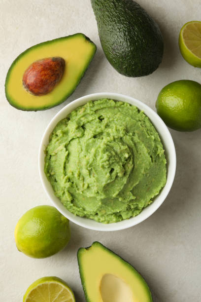 istock Bowl of guacamole, avocado and lime on white textured background, top view 1299750011