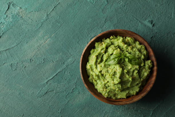 istock Bowl of guacamole on green textured background, space for text 1299750893