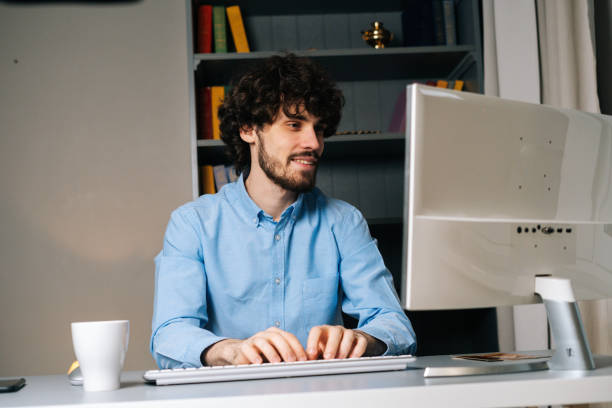 istock Portrait of happy smiling young man using computer and typing online message on wireless keyboard . 1299750993