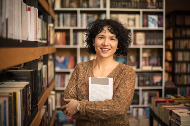 istock Portrait of smiling in library holding a book. Looking at camera. 1299753380
