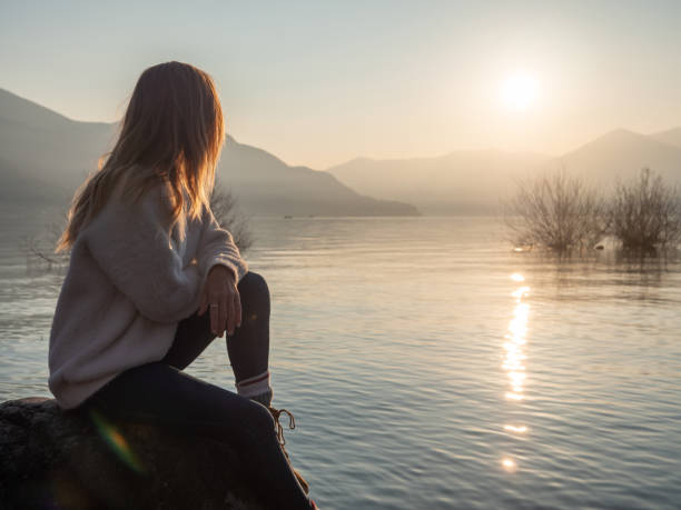 istock Woman contemplates lake at sunset from boulder 1299754281
