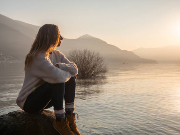 istock Woman contemplates lake at sunset from boulder 1299754482