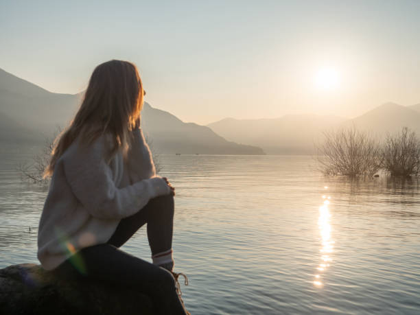 istock Woman contemplates lake at sunset from boulder 1299754557