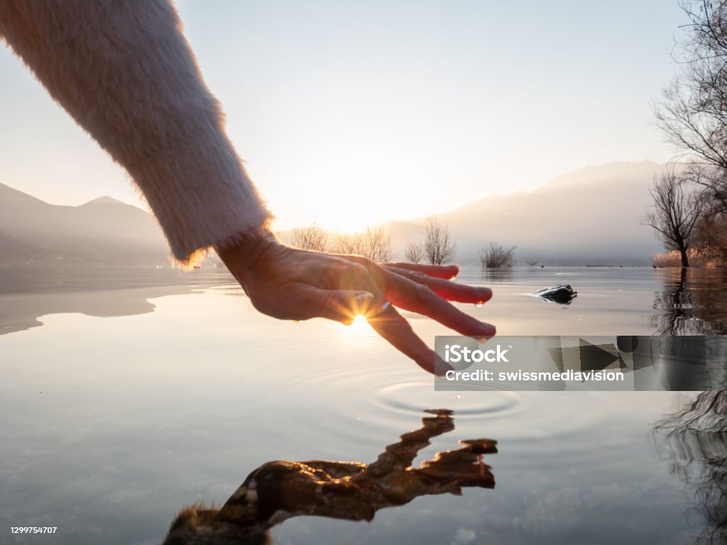 Detail of hand touching water surface of lake at sunset Detail of hand touching and caressing water surface of beautiful lake at sunset, mountain view. Purity freshness clean concept, one person touching lake with hand Water Stock Photo