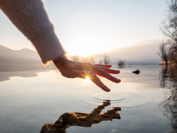 Detail of hand touching water surface of lake at sunset stock photo