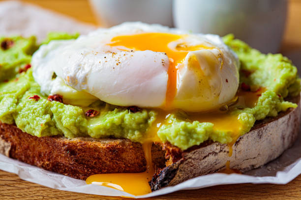 avocado-toast mit pochiertem ei auf holzbrett. frühstückskonzept. - poached stock-fotos und bilder