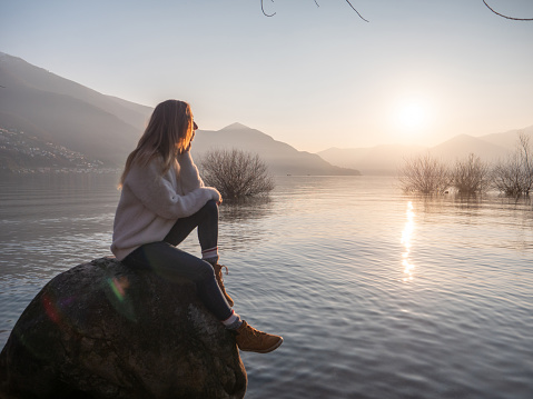 Woman contemplates lake at sunset from boulder