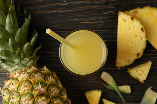 Ripe pineapple and glass of juice on wooden background
