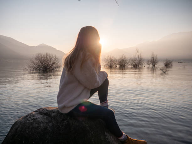 istock Woman contemplates lake at sunset from boulder 1299755376