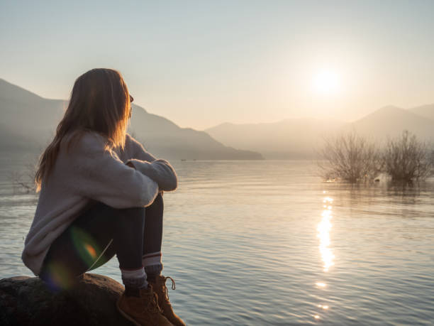 istock Woman contemplates lake at sunset from boulder 1299755877