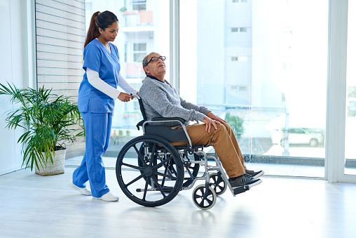 Shot of a young nurse pushing a senior man in a wheelchair