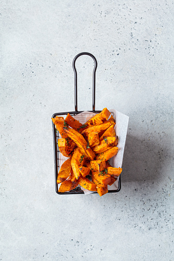 Fried sweet potato wedges in a metal basket, gray background. Vegan food concept.