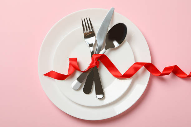 istock Plates with cutlery and red bow on pink background 1299758623