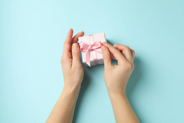 istock Female hands holding gift box with pink ribbon on blue background 1299759387